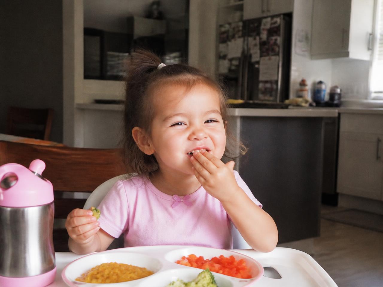 Menina de 3 anos sorrindo enquanto come refeição vegetariana colorida